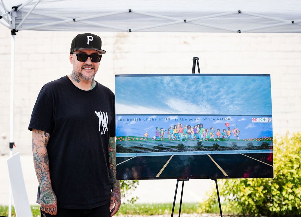 Flint Public Art Project artist Johnny Fletcher stands next to the rendering of the mural he created for the Buick Gallery wall.
