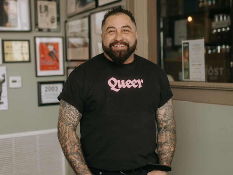 Wearing a prominent "Queer" shirt, Mason Gallo is all smiles inside Queens' Provisions in downtown Flint on May 4, 2024.
