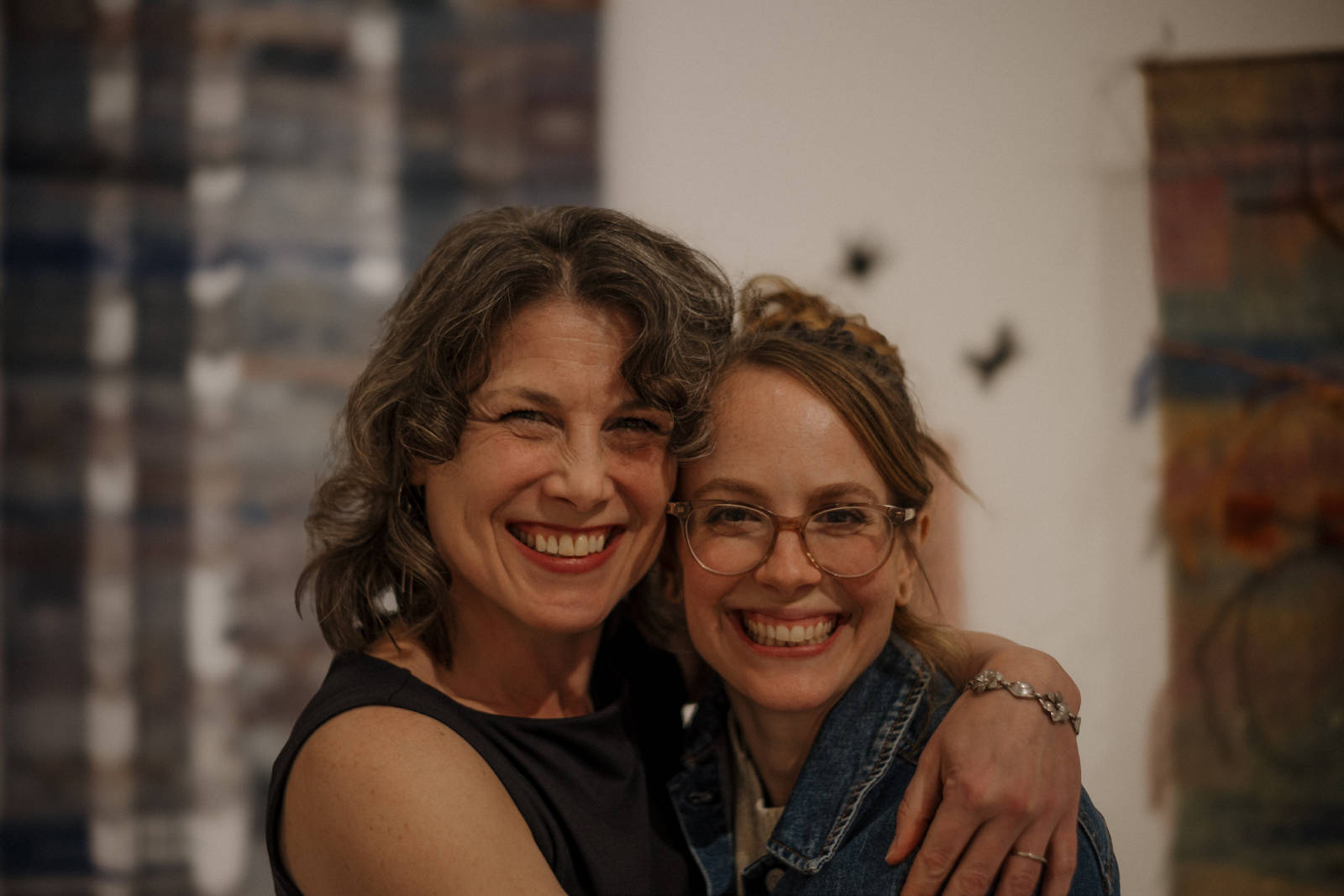 "I always tell people that every day is different and unexpected here. You never know what stories you’re going to hear or what you’re going to get from the artwork,” explains Katie Cotton in a warm embrace with Michele Leclaire inside Buckham Gallery on April 18, 2024. (Anthony Summers | Flintside.com)
