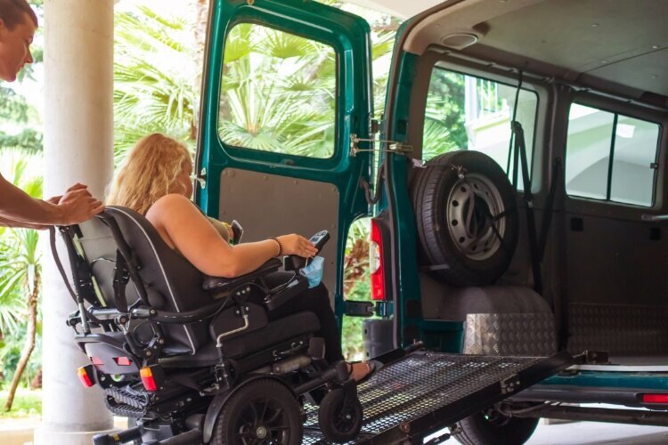 Photo shows a woman using a wheelchair being pushed up a ramp into an accessible van.