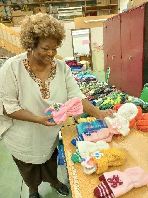 Rosie Ray-Henderson holds fleece hats and mittens. “I coordinate colors and embellish with a button to make the flower pop!” she exclaimed. (Sherrema A. Oom-Dove | Flintside)

