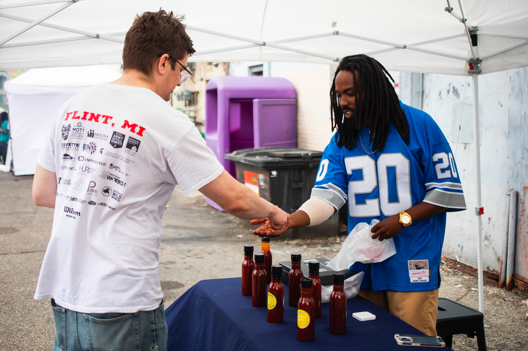 Jon Davis of Flint, right, sells a bottle of his homemade barbecue sauce, called Brotha J's, to Kyle Nicolay of Davison, left, as hundreds of people gather in downtown Flint's Buckham Alley for Alley Fest on Saturday, July 8, 2023. (Katy Kildee | Flintside)