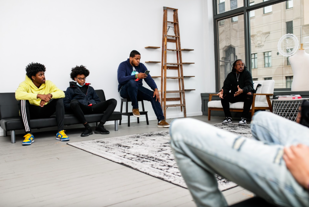 Three young men from the Boys & Girls Club sit and listen to co-owner Lee Grant Allen share his personal journey on Tuesday, May 2, 2023, at BAU-HOUSE in downtown Flint. (Jenifer Veloso | Flintside)