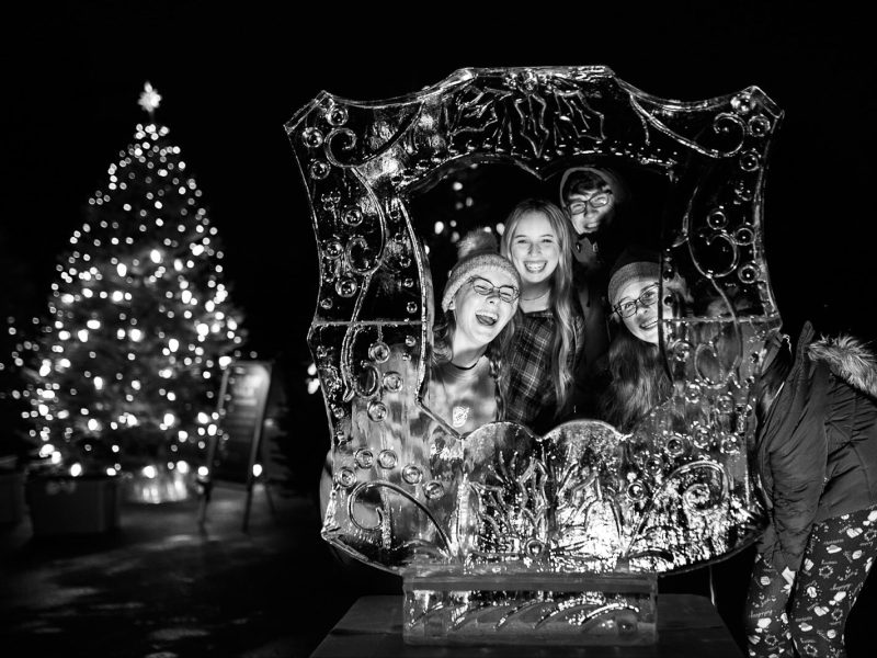 Guests at Applewood smile together for a picture next to an outdoor ice sculpture during the College Cultural area’s 37th Annual Holiday Walk in Flint on Tuesday, Dec. 6, 2022.