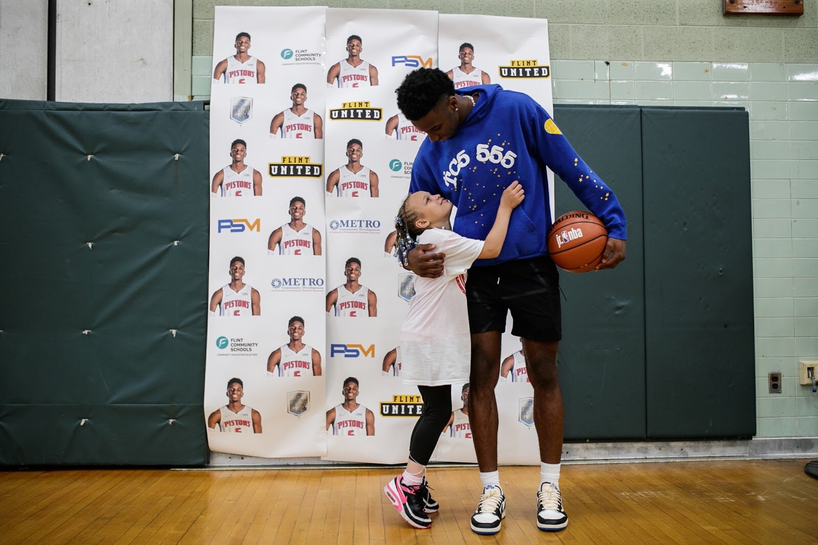 A child hugs Hamidou Diallo before taking a portrait with him during Hami Day Camp at Northwestern High School in Flint, on Friday, Aug. 27, 2022.  (Jenifer Veloso | Flintside.com)
