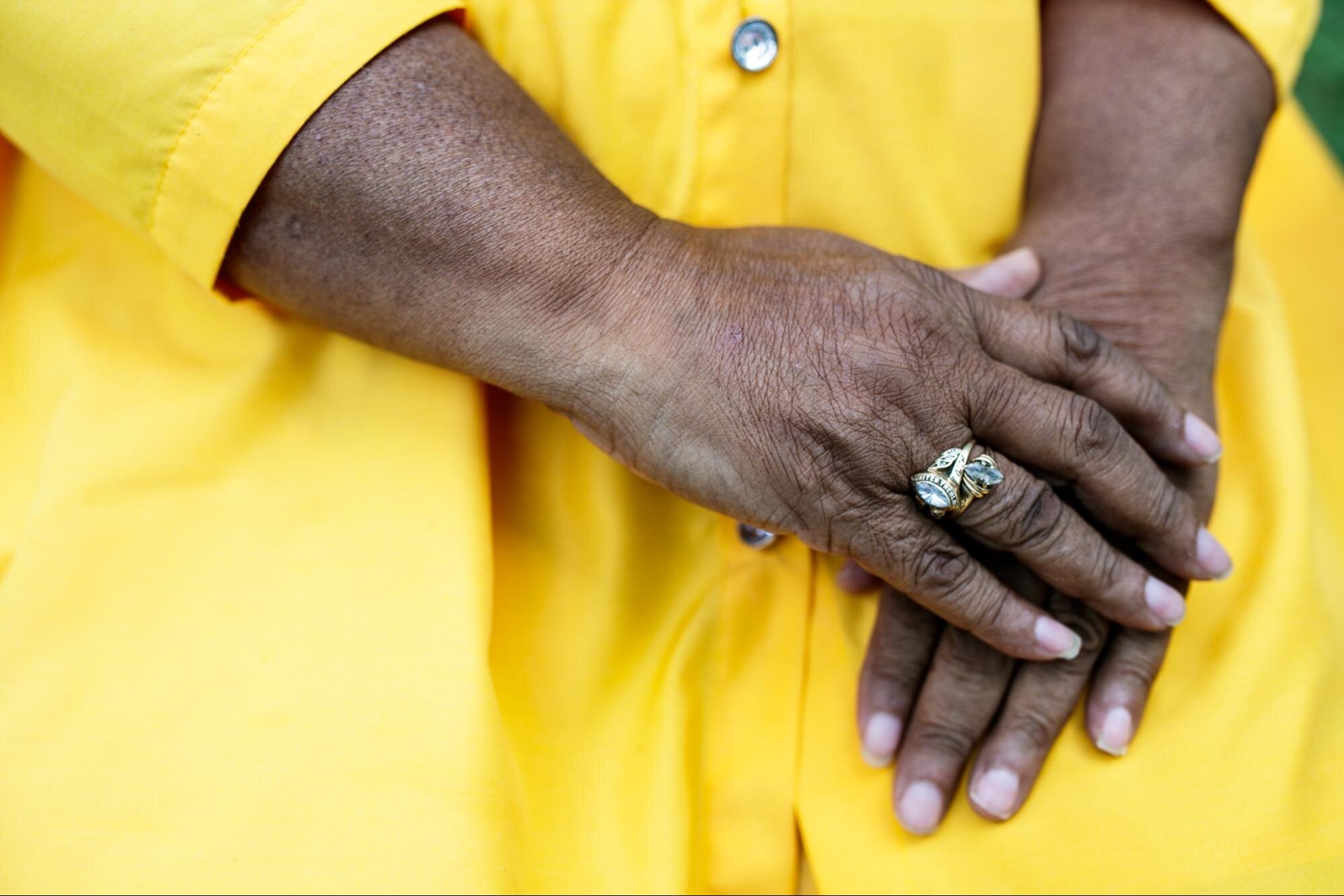 Victoria McKenze rests her hands on her lap showing two rings of significance. One ring celebrates her graduation from the University of Michigan-Flint’s Bachelor of Arts in Criminal Justice in 1995, and the other is for her Master of Divinity from the United Theological Seminary in 2000.