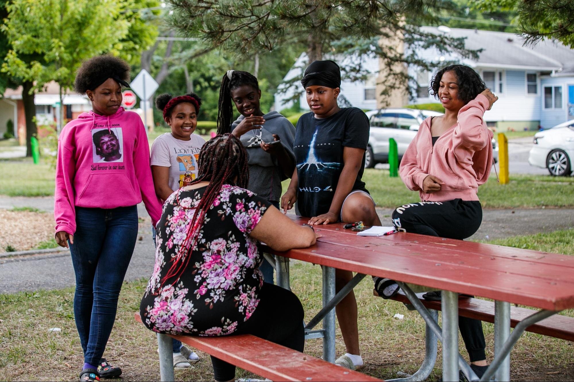 Honny Williams sits on a park bench while talking to neighborhood kids (pictured from left to right; Terynn Henry, Sakara Johnsonn, Nene, Miesia Leroy, Nikiyah Johnson) in Sarvis Park, Flint, on July 26, 2022. (Jenifer Veloso | Flintside.com)