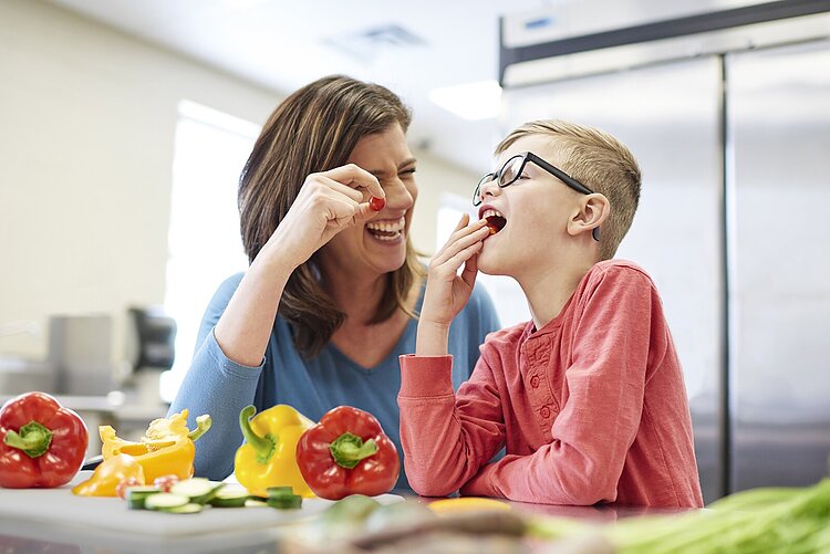 A mom and son taste fresh vegatables.
