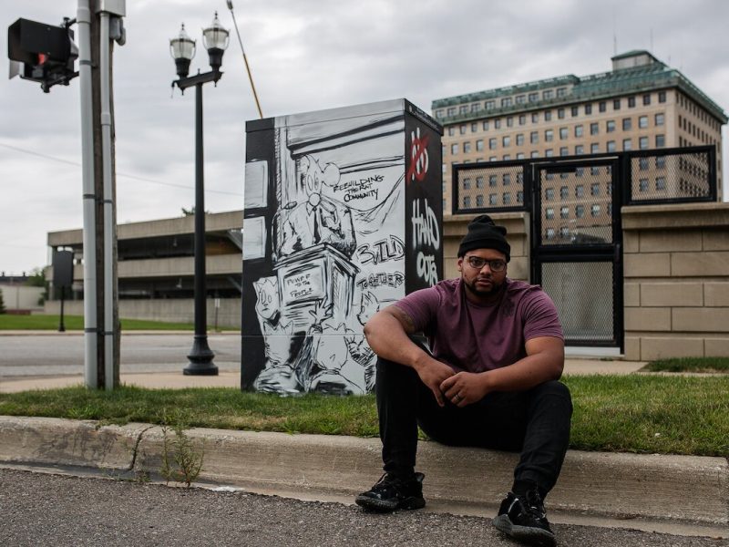 Keyon Lovett, the ArtSchool Dropout, sits in front of an electrical box he was commissioned to design downtown Flint.