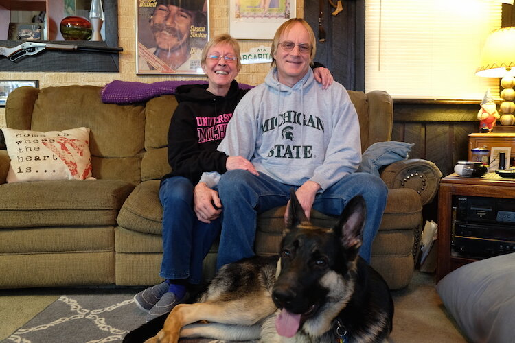 Nancy and Jim Gallagher sit in their living room with their fur baby Mijo.