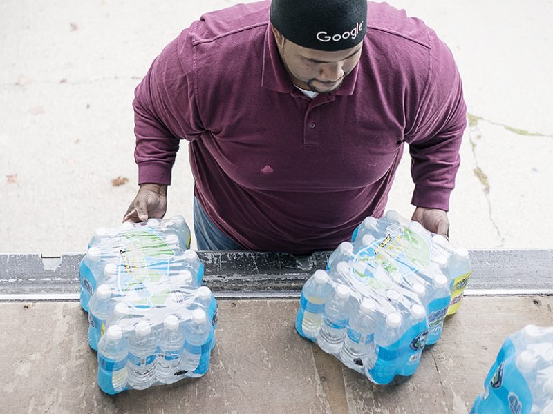 William Harris, 31, of Flint, slides two cases of water off the back of his team's delivery truck on Flint's eastside. The team from Asbury United Methodist deliver water to 60 to 70 homes on their route.