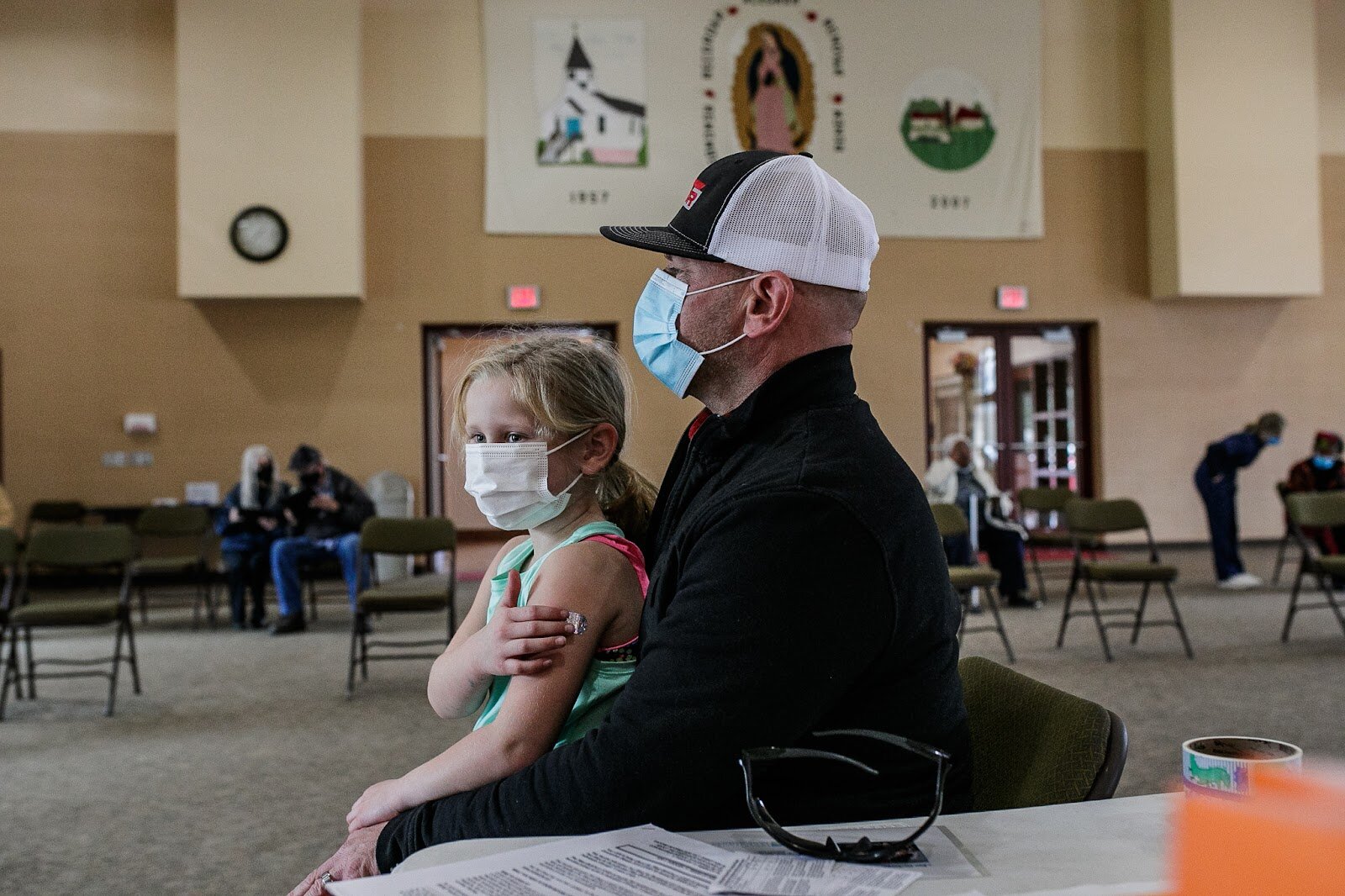 Marin Derwin (age 6) receives her first Pfizer COVID-19 vaccine while sitting on her father's lap.