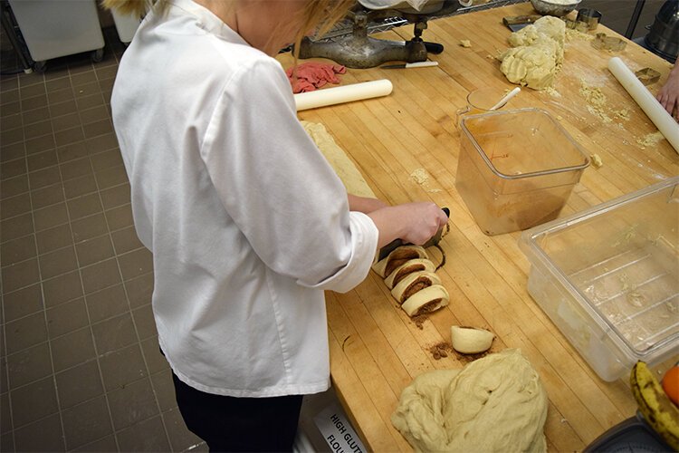 Lakeville High student Mina Whitehead cuts a cinnamon roll she's made into more manageable pieces. 