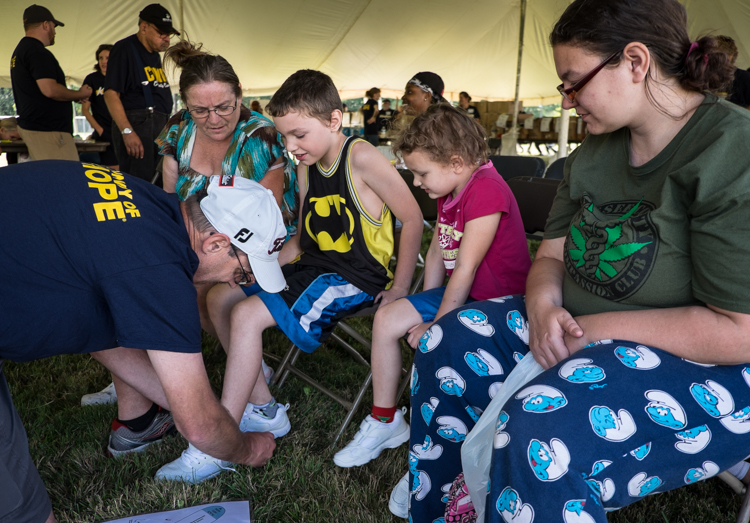 Brent Rhoads of Midland assists Benjamin Huff, 8, and Thea Huff, 5, with new shoes at the Convoy of Hope event in Bassett Park in Flint on Saturday. At right is Leanne Talada of Burton, the children's mother. In background is family friend Susan Luar