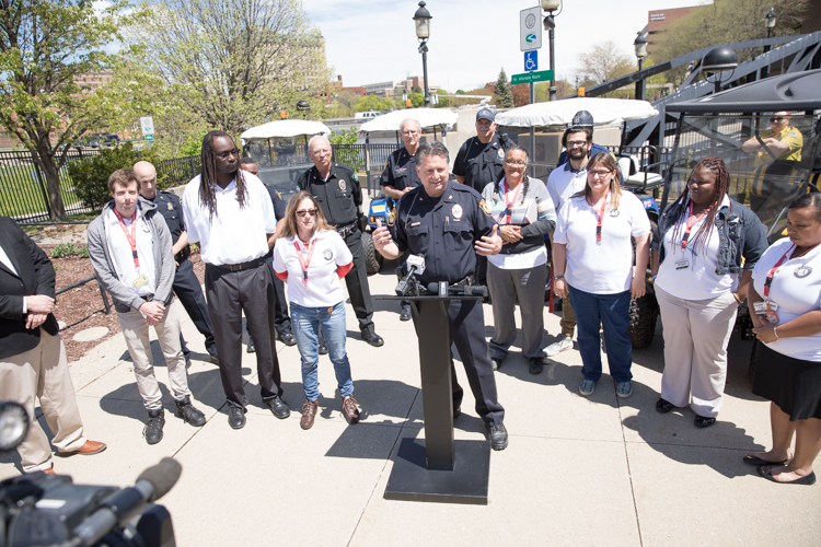 UM-Flint Police Chief Ray Hall (center) speaks at a press conference about the many partners that have come together to make the Flint River Watchers program successful. Now in its second year, AmeriCorp workers and volunteers patrol the river, clean up debris, talk to residents, and pass out dog treats. 